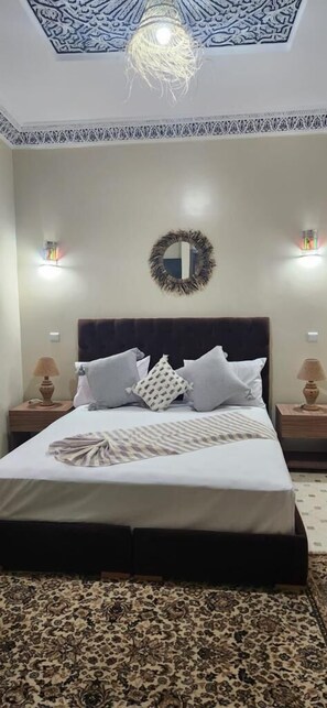 A bedroom with a large bed, a decorative ceiling, a mirror, and two bedside lamps.