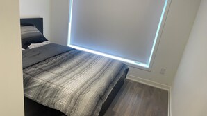Makuuhuone, jossa on sänky, ikkuna, jossa on sälekaihtimet, ja puulattia.