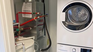 Pesuhuoneessa on kaksi päällekkäin asennettua etukuormauspyykinpesukonetta, lämminvesivaraaja sekä erilaisia putkia ja venttiilejä.