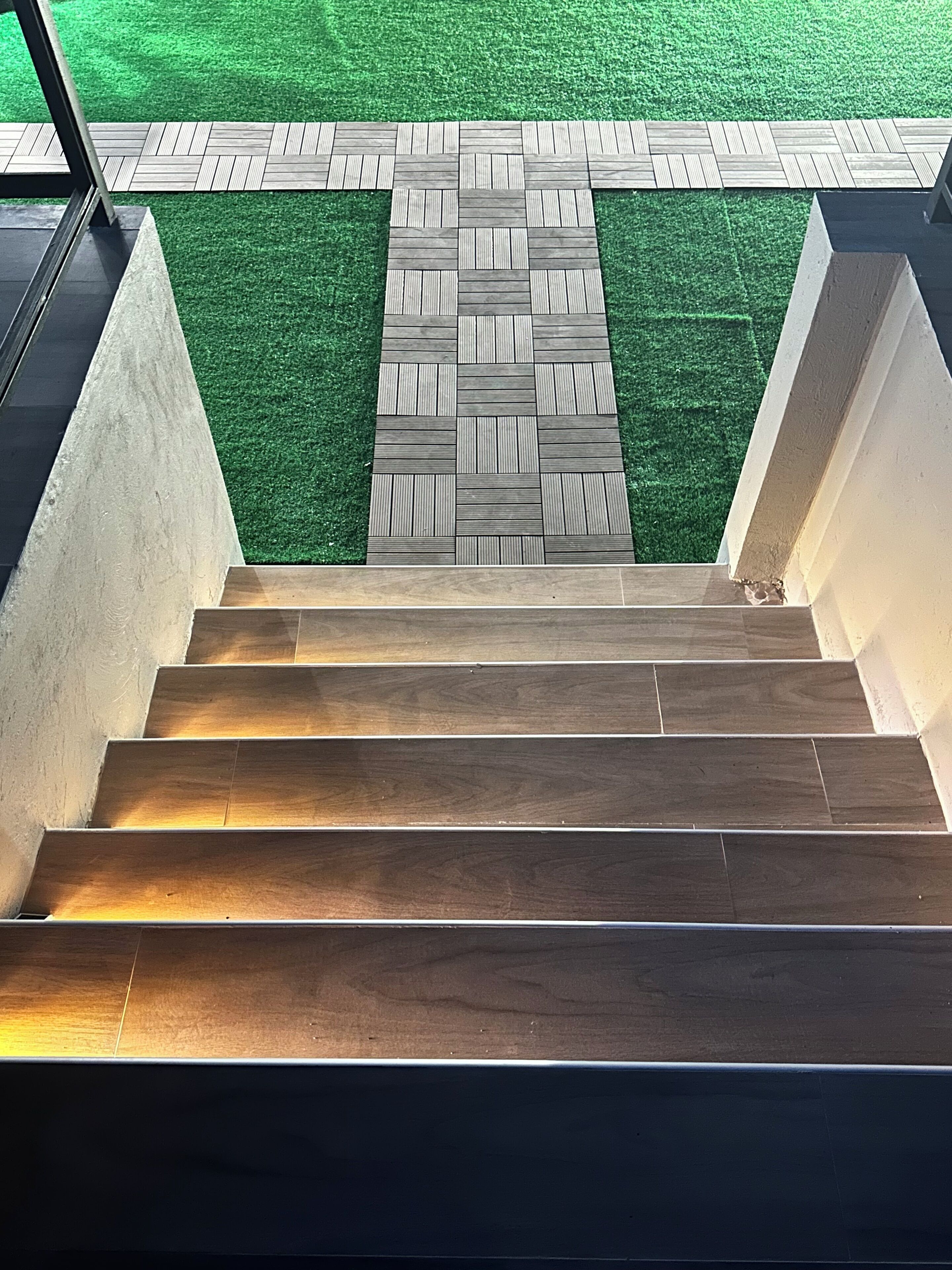 Un escalier en bois mène à un espace recouvert d’une moquette d’herbe artificielle verte.
