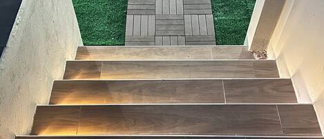 A wooden staircase leading to a green artificial grass area.