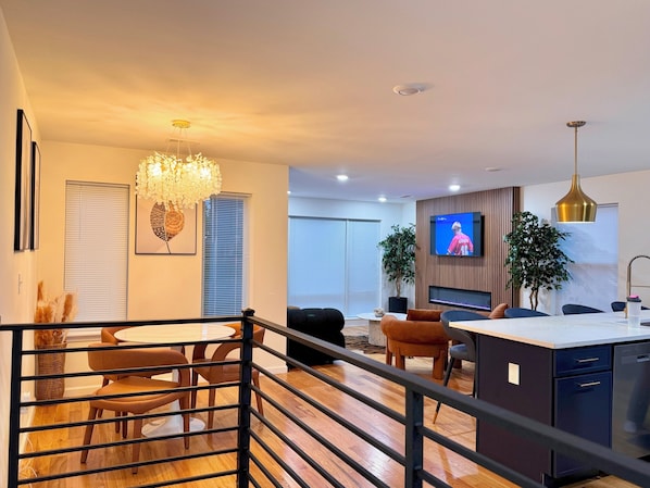 Uma sala de estar moderna com área de jantar, TV fixada na parede e escada para outro andar.