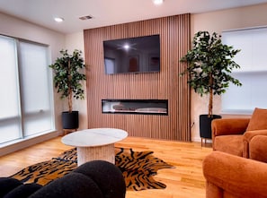 Uma sala de estar moderna com uma televisão de tela plana fixada numa parede de madeira, uma mesa de centro redonda e dois sofás.