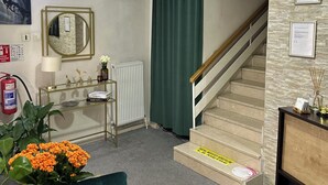 A hotel lobby with a staircase, a reception desk, a console table with decorative items, a green chair, and a fire extinguisher. - Diva Otel (Isparta)