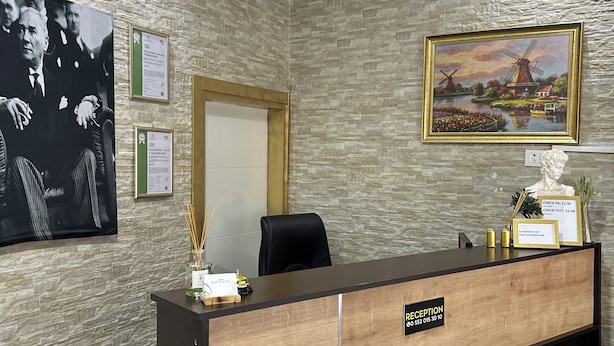 A reception desk with a wooden finish, a black chair, and a framed painting of a windmill. - Diva Otel (Isparta)