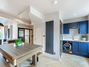 Eine moderne Küche mit blauen Schränken, einer integrierten Waschmaschine und einem Essbereich mit Holztisch und Topfpflanzen.