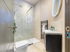 A modern bathroom with a glass-enclosed shower, a white toilet, a black cabinet with a sink, and a towel rack.