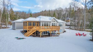 Una casa de dos pisos con un balcón de madera y un porche cubierto, rodeada de nieve y árboles.