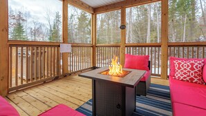 Una terraza de madera con un hogar, un sofá y vistas a árboles.