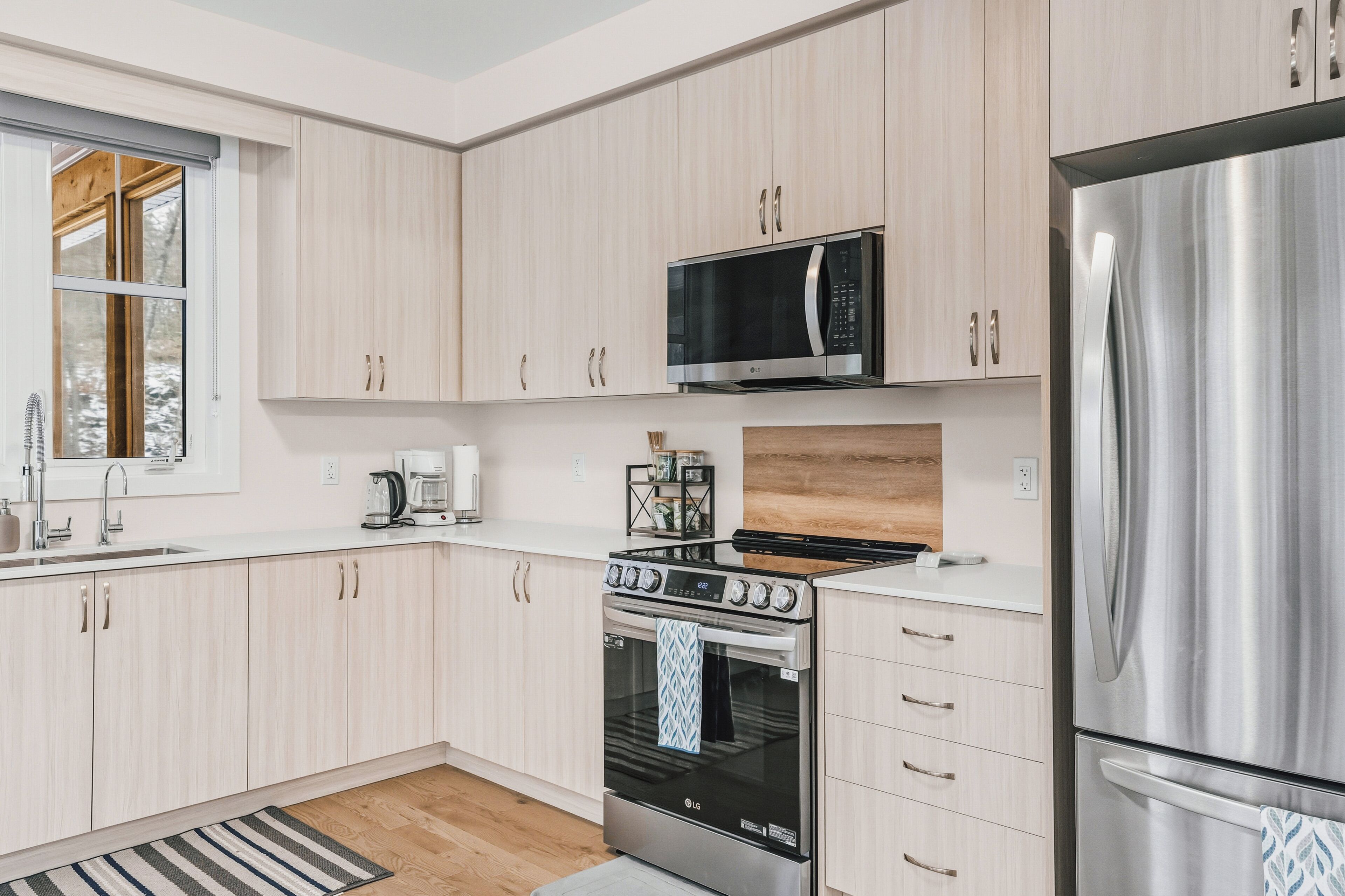 Eine moderne Küche mit hellen Holzschränken, Edelstahlgeräten, einer eingebauten Mikrowelle, einem Gasherd und einem großen Kühlschrank.