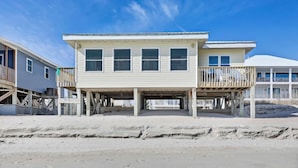 Una casa frente a la playa con un porche cubierto y un balcón.