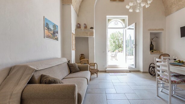 A cozy living room with a sofa, a dining table, and a chair. There is a window with a view of the outdoors.