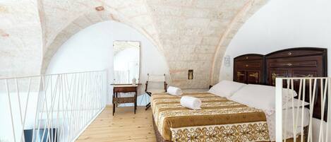 Quarto com piso de madeira, cama com colcha estampada, mesa de cabeceira, espelho e guarda-roupa de madeira.
