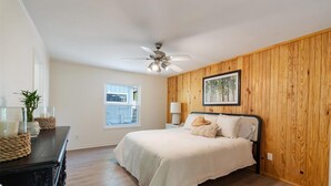 Une chambre à coucher avec un lit, des murs en bois, un ventilateur de plafond, une fenêtre et une table de chevet avec une lampe.