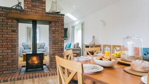 A cozy living area with a brick fireplace, a dining table set with breakfast, and a comfortable seating area. - Bwthyn Alberts -  an on the beach that sleeps 7 guests  in 3 bedrooms (Trearddur Bay)