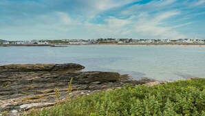 A coastal view with rocky shoreline, clear water, and a distant residential area. - Bwthyn Alberts -  an on the beach that sleeps 7 guests  in 3 bedrooms (Trearddur Bay)