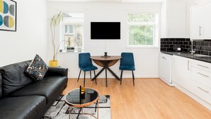 Uma sala de estar moderna com um sofá de couro preto, duas poltronas azuis, uma mesa de centro redonda e uma TV na parede.