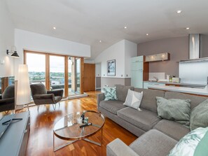 Una sala de estar moderna con una mesa de centro de vidrio, sofás grises y vistas a través de puertas correderas de cristal.