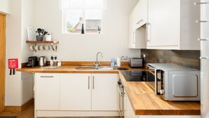 Una cocina moderna con armarios blancos, encimera de madera, pileta de acero inoxidable, un tostador y una tetera.