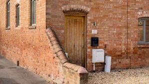 Un edificio de ladrillo con puerta de madera, un buzón pequeño y un cartel que dice 'The Tack Room'.