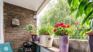 A balcony with a brick wall, a metal chair, a grill, and potted plants with red flowers. - Peaceful, zen apartment with parking, Kew, London - Pass the Keys (Richmond)