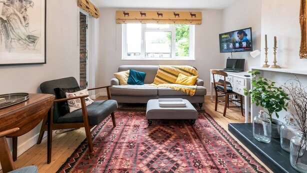A cozy living room with a sofa, a wooden coffee table, a patterned rug, a television, and a chandelier. - Peaceful, zen apartment with parking, Kew, London - Pass the Keys (Richmond)
