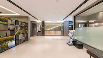 A modern hotel lobby with a reception desk, seating area, and a glass wall.