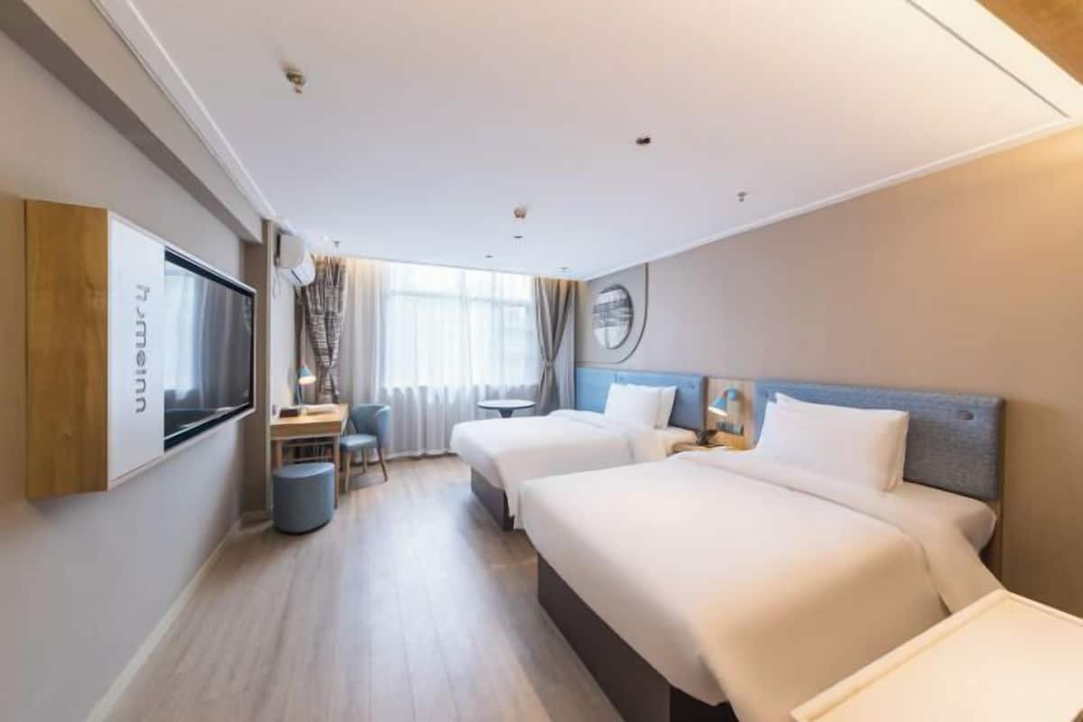 A hotel room with two beds, a desk, a chair, and a TV.