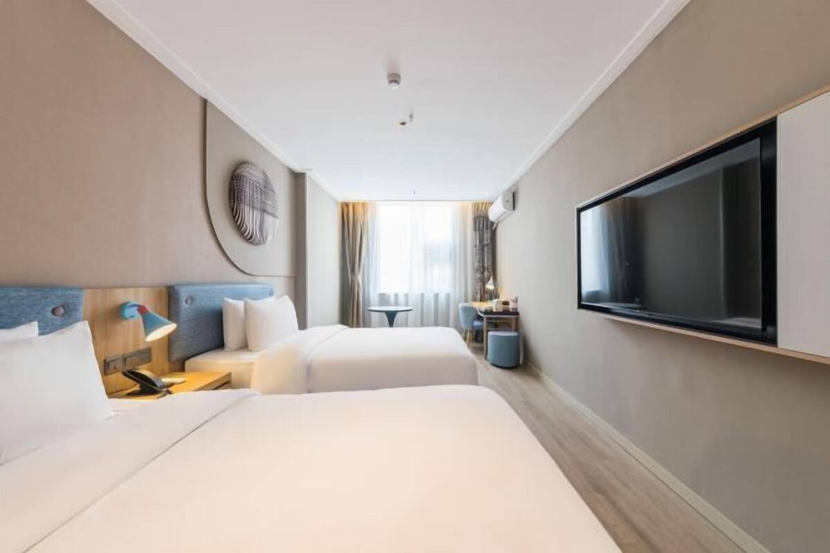 A hotel room with two beds, a TV mounted on the wall, a desk, and a small table.