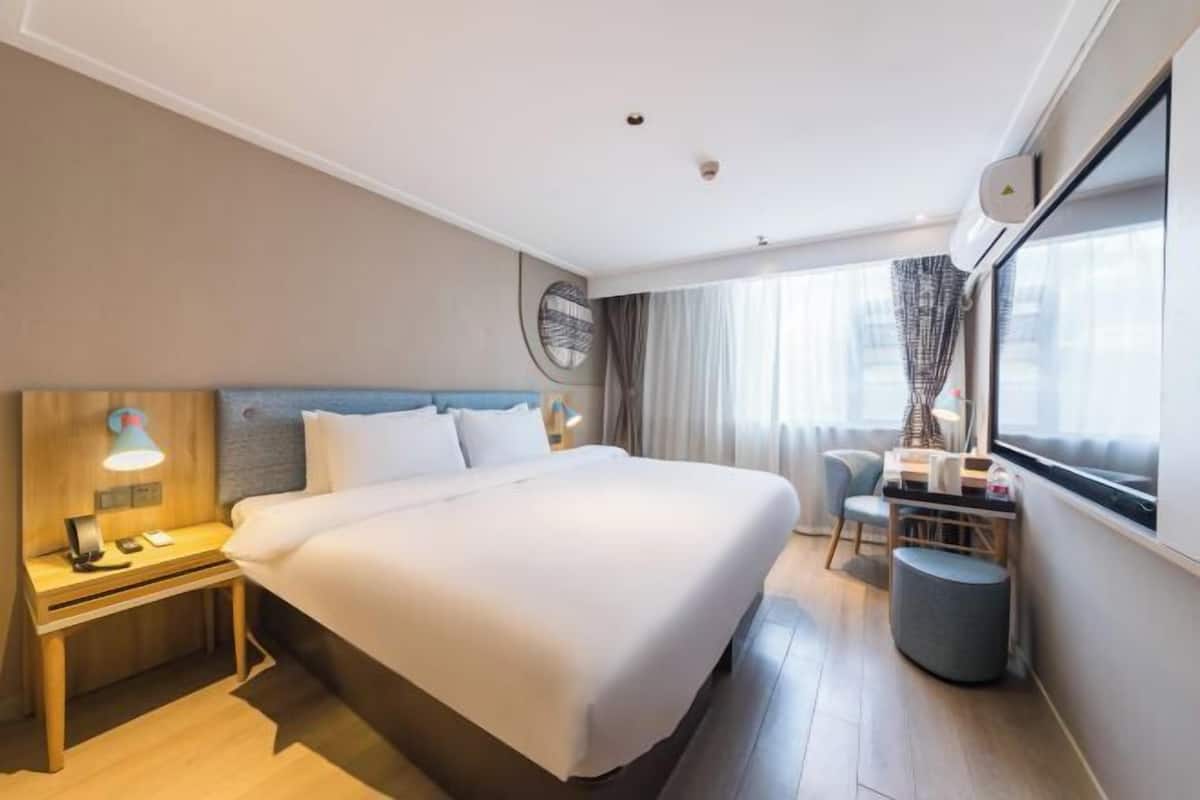 A hotel room with a large bed, bedside table with lamp, and a small desk with chair.