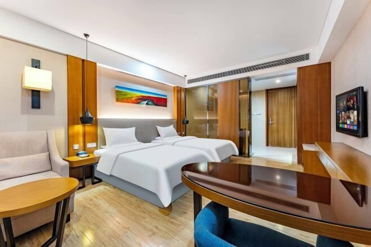 A modern hotel room with a bed, bedside table, lamp, and a view of the city.