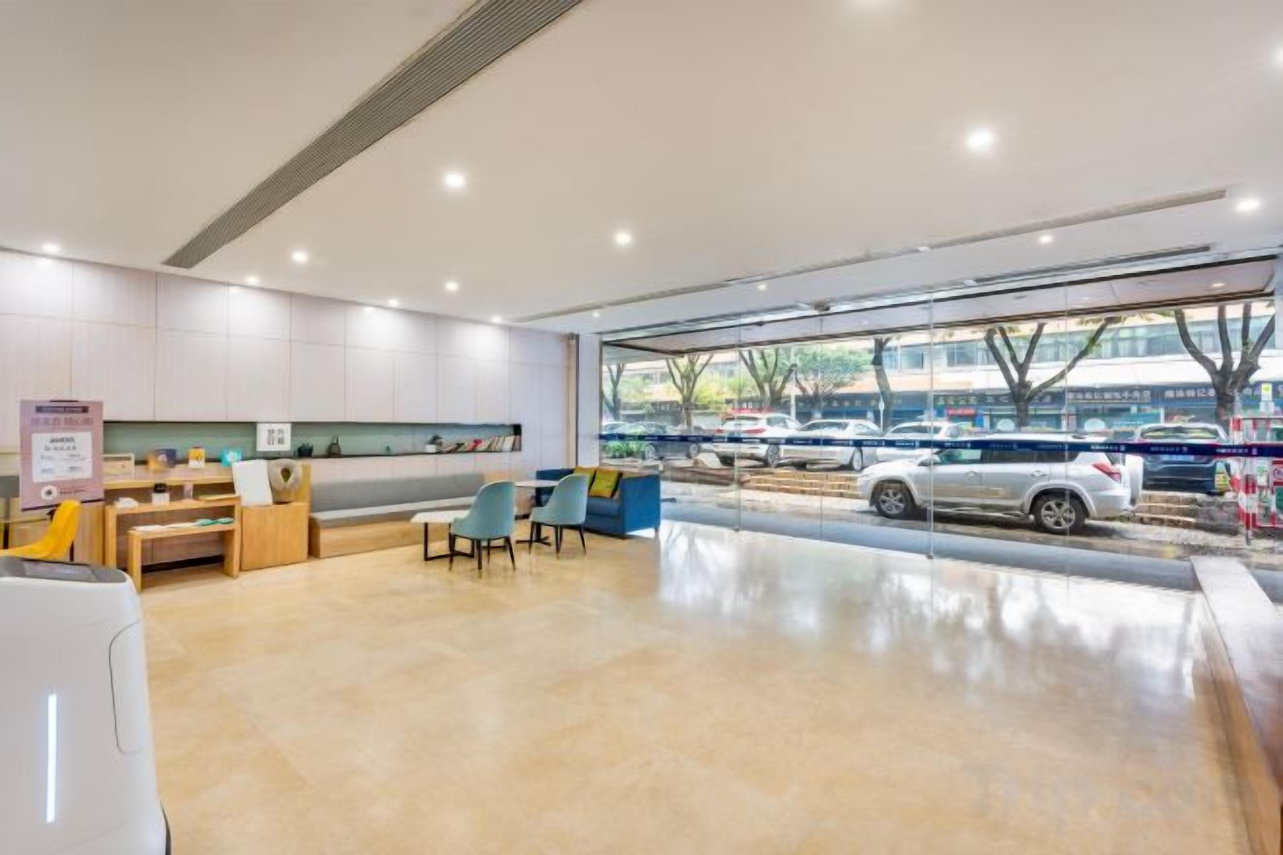 Un área de recepción moderna con zona de estar, mostrador de recepción y vista a coches estacionados afuera.