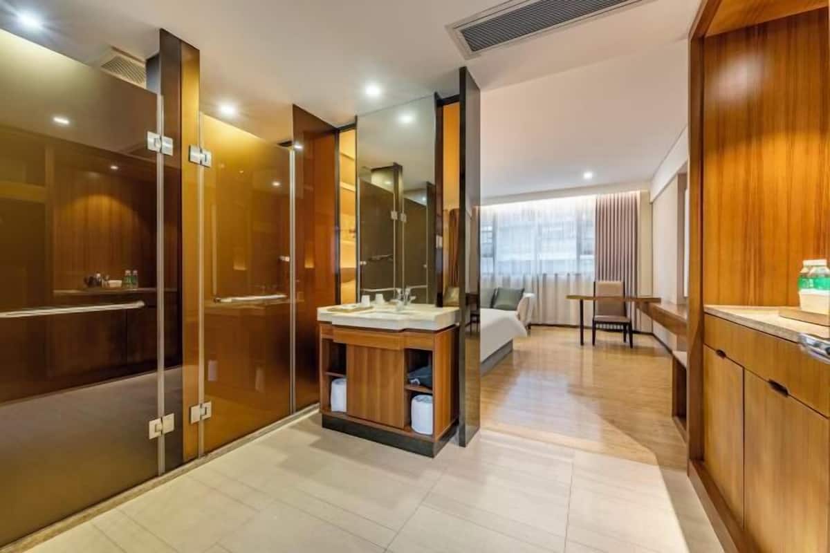 A modern hotel room with a wooden vanity, a glass shower enclosure, and a bed with a view.