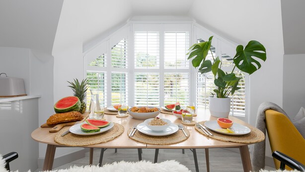 Ein Essbereich mit einem Tisch, der für ein Frühstück gedeckt ist, darunter Teller mit Speisen, eine Schüssel und ein Blumentopf.