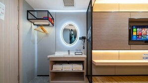 A modern bathroom with a vanity, a round mirror, a shelf with towels, and a wall-mounted TV.