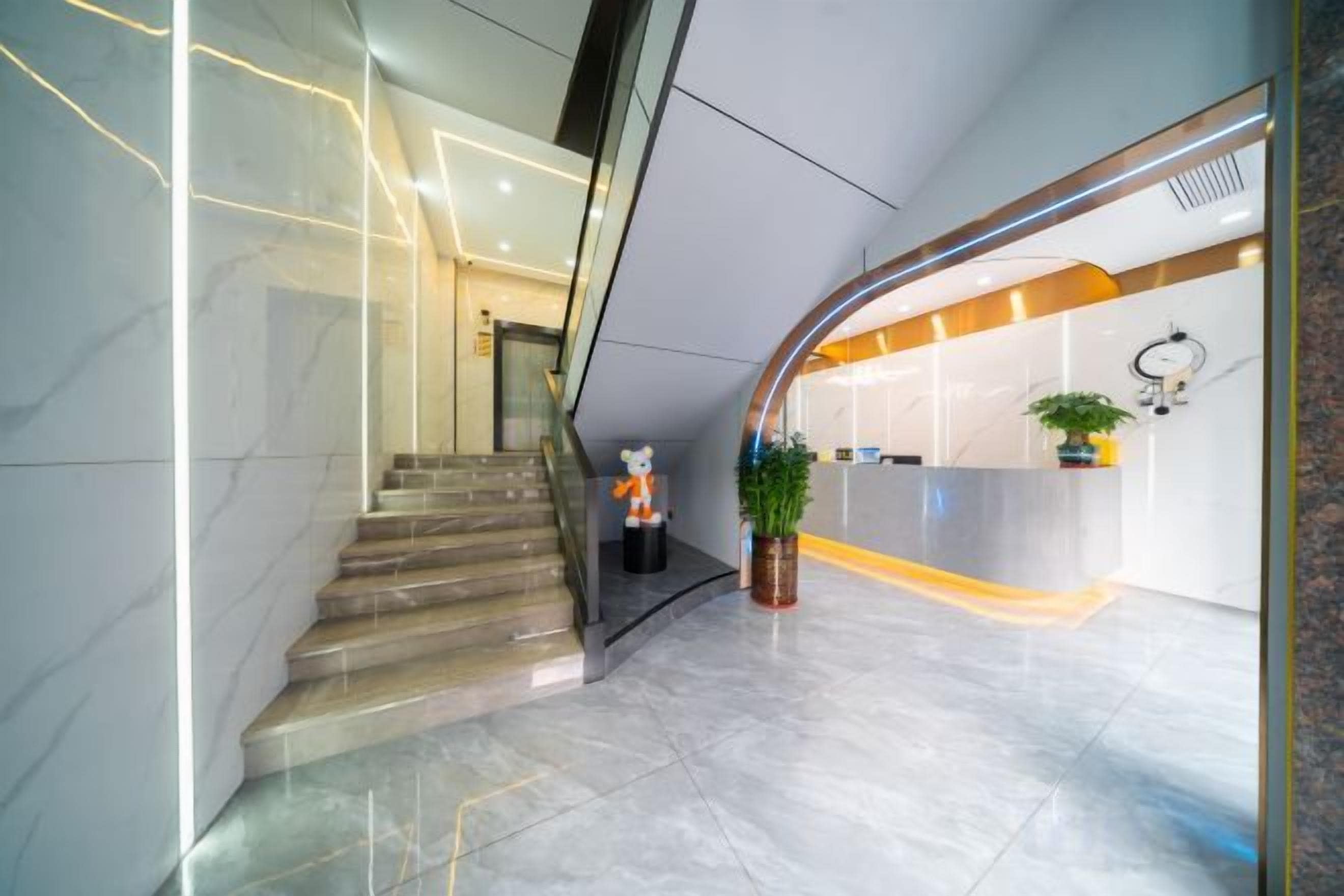 Um hall de hotel moderno com uma escadaria de mármore, balcão de recepção e um vaso de planta.