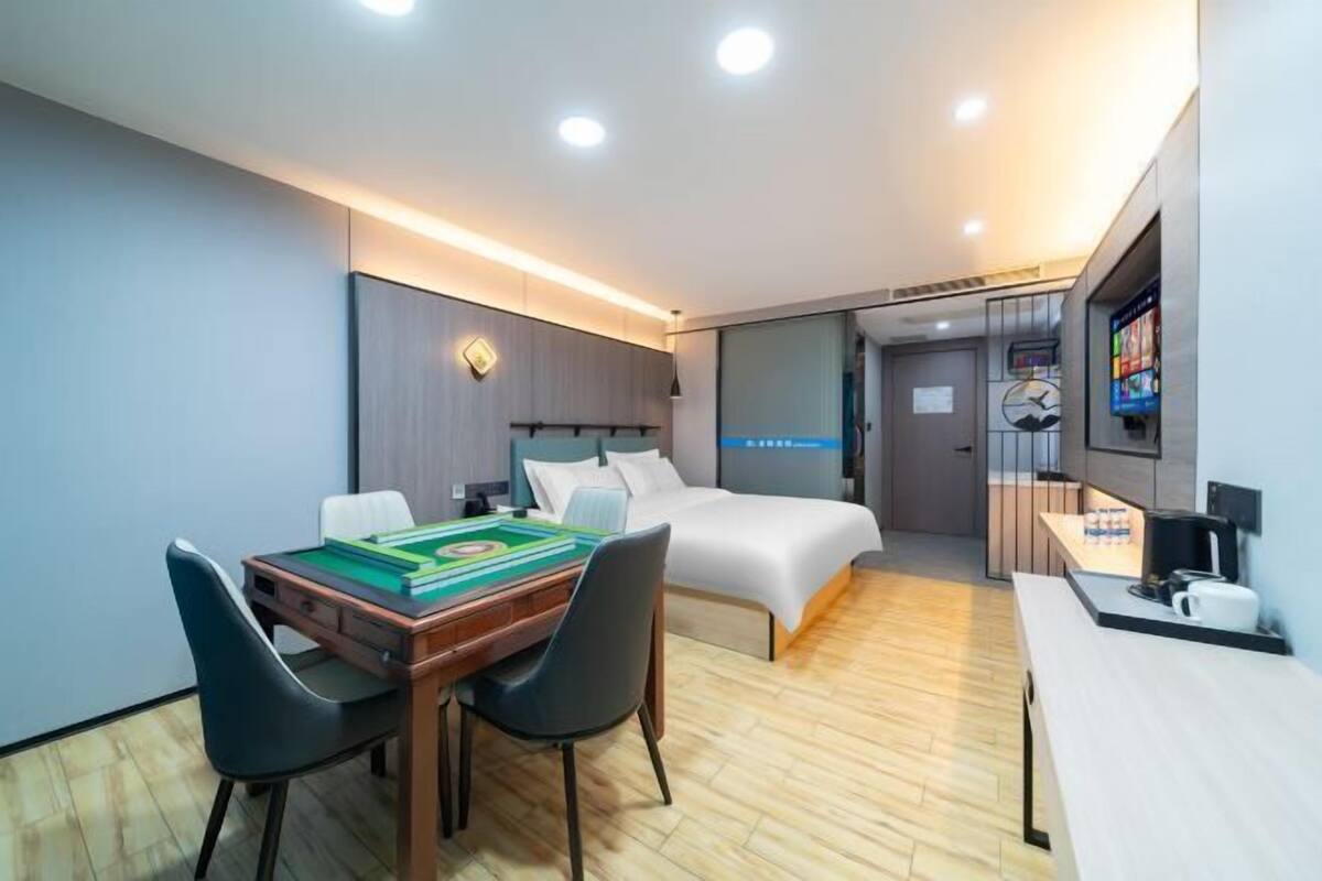 A modern hotel room with a bed, a desk, a chair, a board game, and a TV.