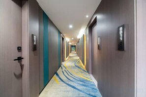 Een hotelgangen met deuren, een vloerbedekking en lichtschakelaars aan de muur.