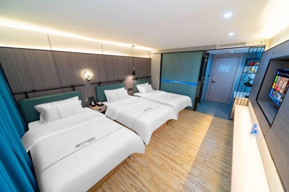 A hotel room with three beds, a TV, and a minibar.