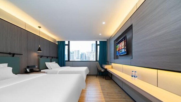 A modern hotel room with two beds, a desk, and a TV mounted on the wall.