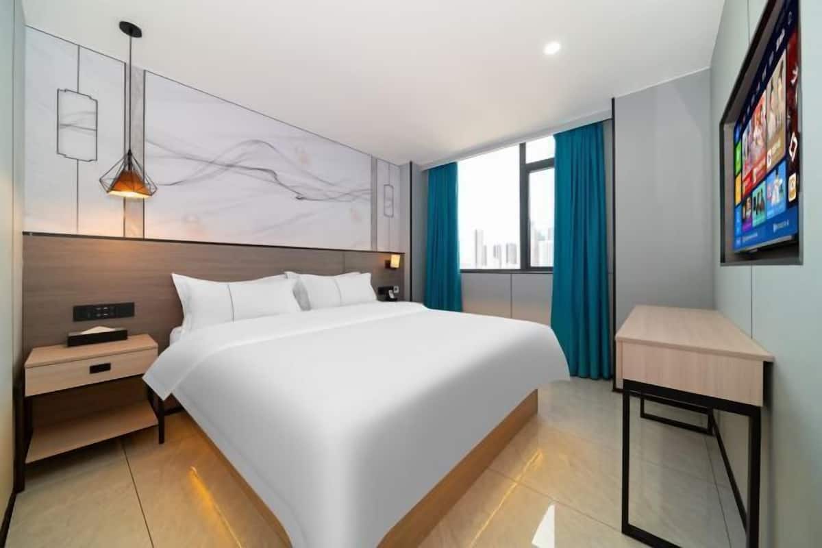 A modern hotel room with a large bed, bedside tables, a desk, a wall-mounted TV, and a city view.