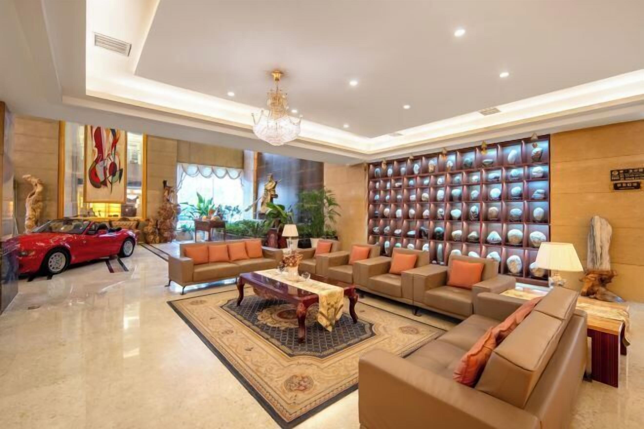 A spacious lobby with a red convertible, leather sofas, a chandelier, and a wall of decorative items.