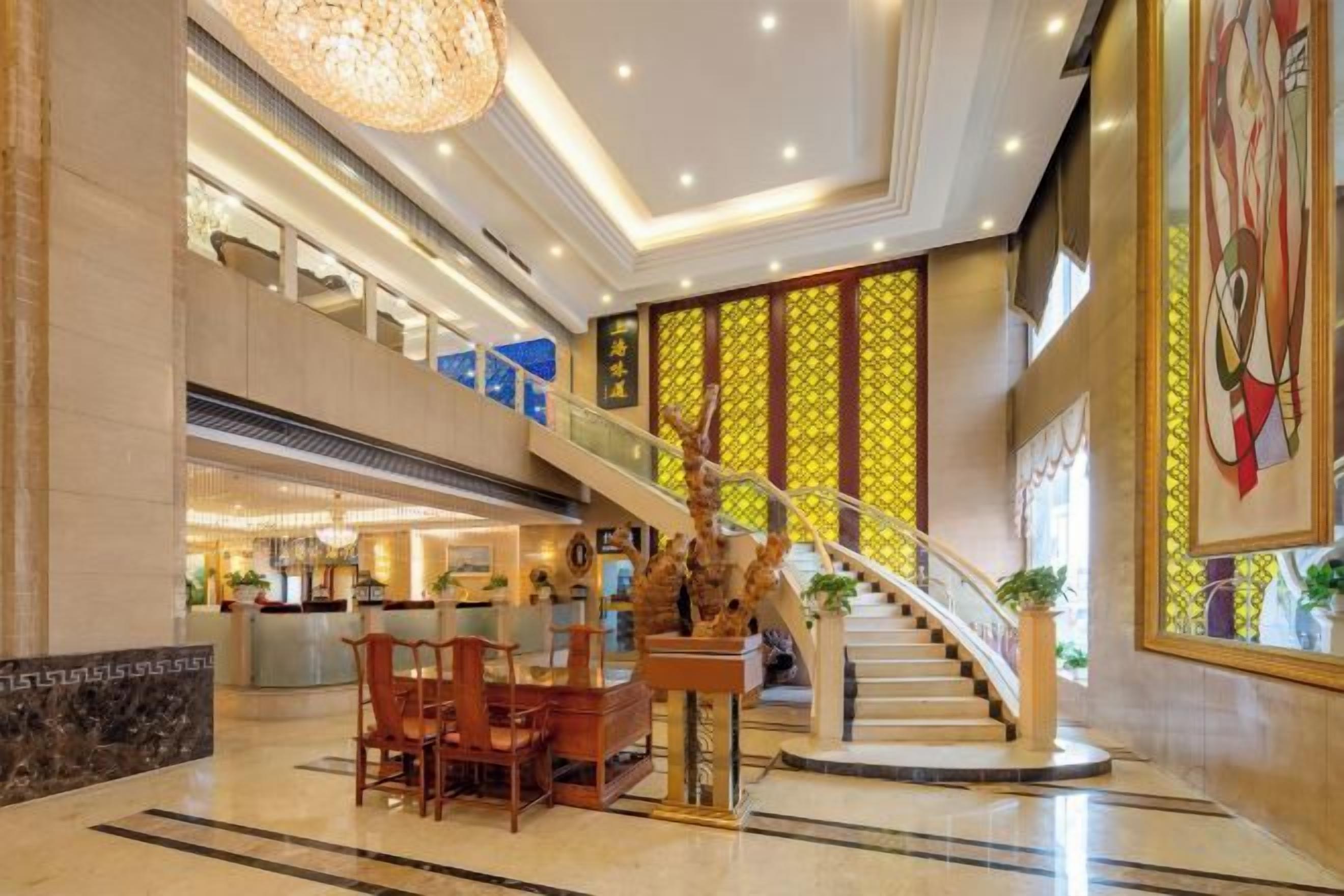 Un vestíbulo de hotel con una escalera monumental, un mostrador de recepción y un área de descanso.