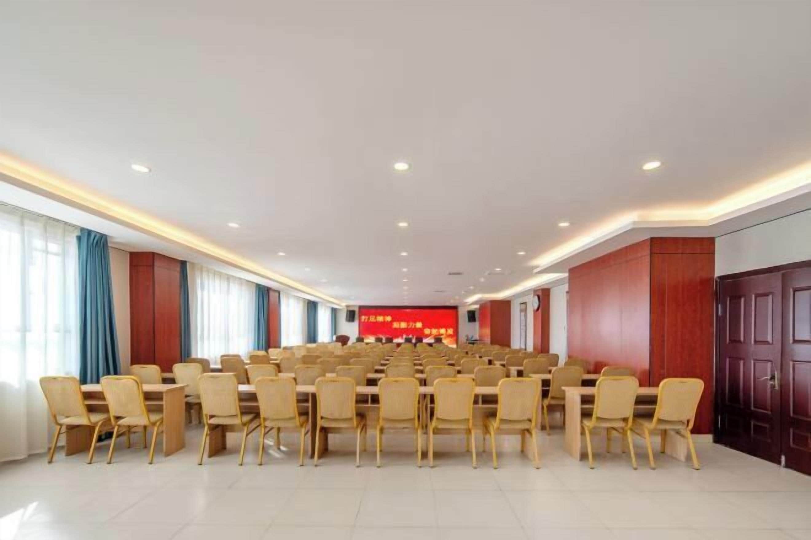A conference room with rows of tables and chairs, a red screen with text, and wooden paneling on the walls.