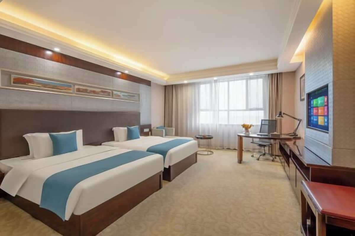Ein Hotelzimmer mit zwei Betten, einem Schreibtisch, einem Stuhl, einem Fernseher und einem Fenster mit Vorhängen.