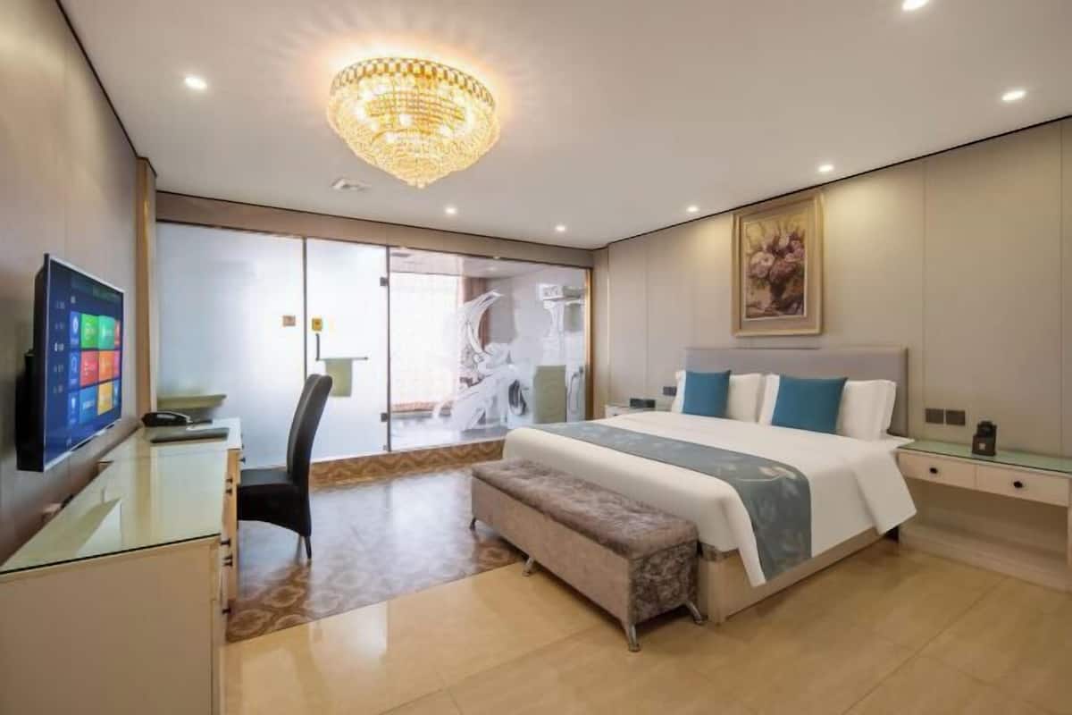 Ein modernes Hotelzimmer mit einem großen Bett, einem Schreibtisch mit Computer, einer Bank und einer Kristallleuchtre.