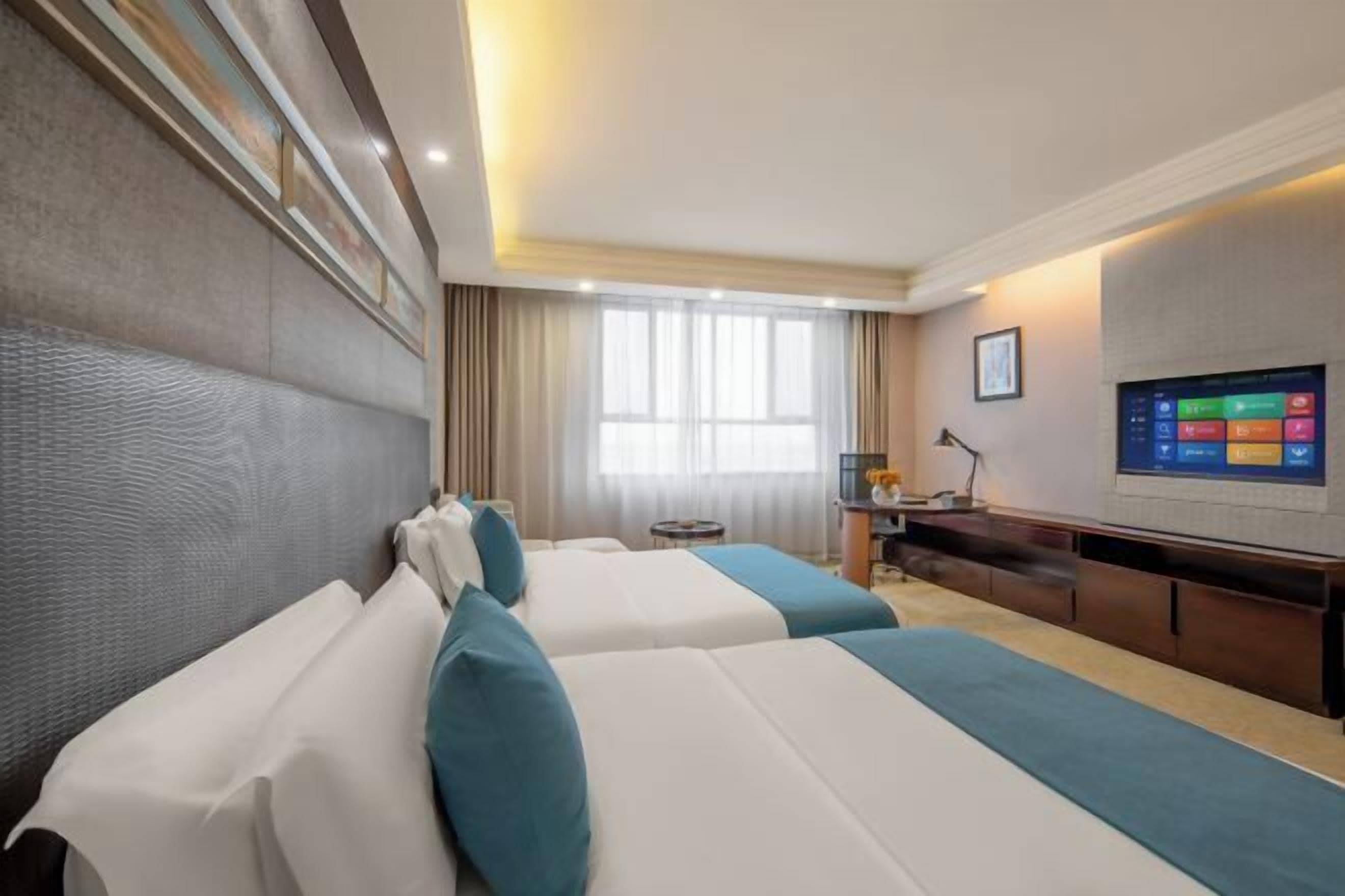 A hotel room with two beds, a desk, a TV, and a window with curtains.