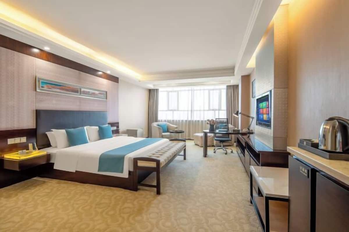 Ein Hotelzimmer mit Bett, Schreibtisch, Stuhl, Fernseher und einer Küchenzeile.