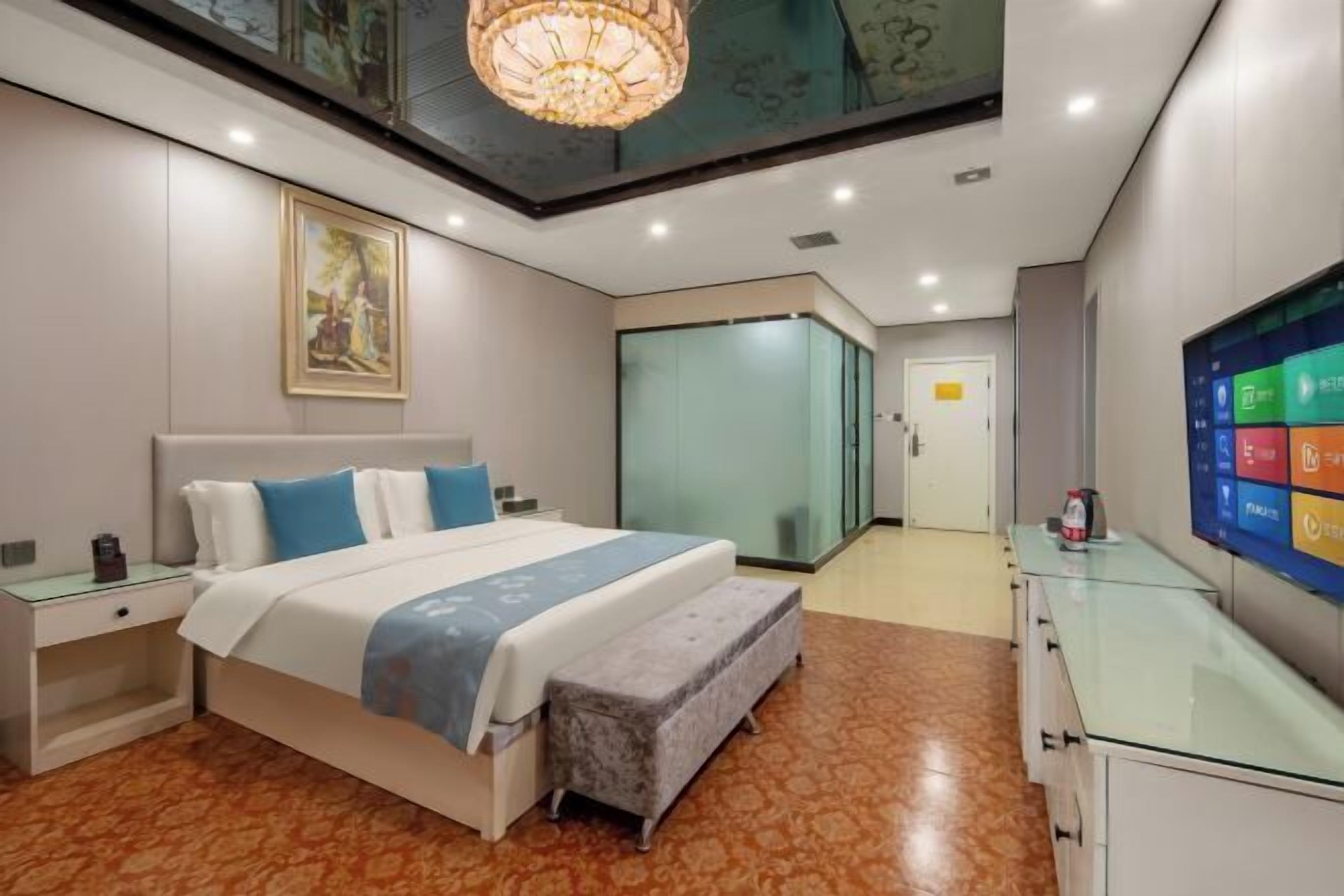 A modern hotel room with a bed, bedside tables, a bench, a TV, and a glass cabinet.