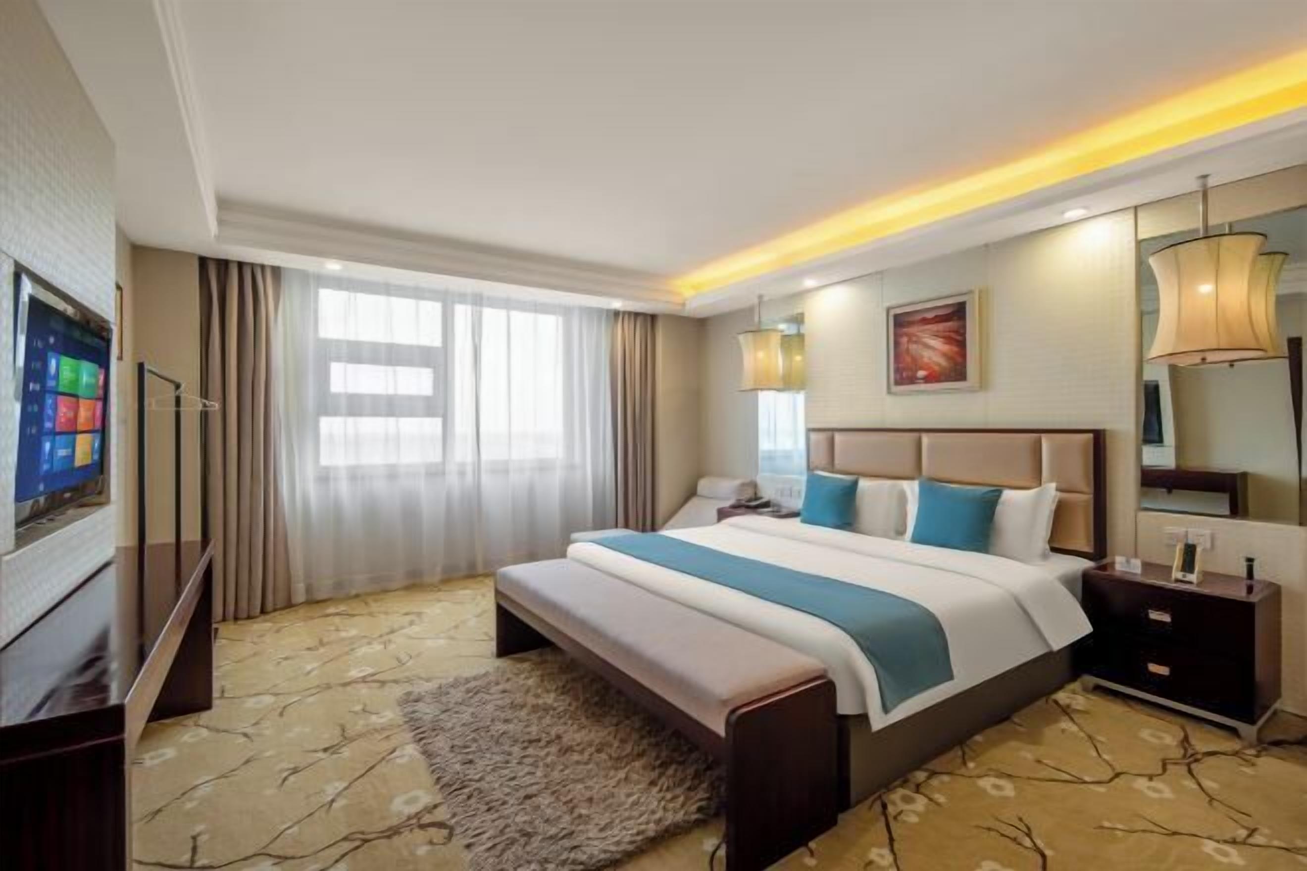 A hotel room with a large bed, bedside tables, a TV, and a window with curtains.